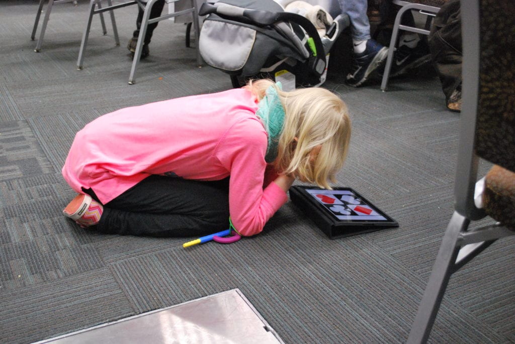Blond girl kneeling on floor looking at an iPad.