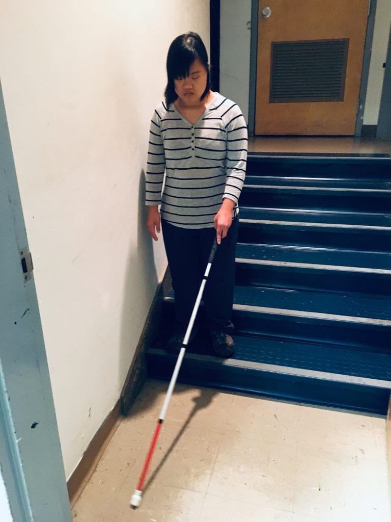Girl reaching the bottom of stairs using white mobility cane